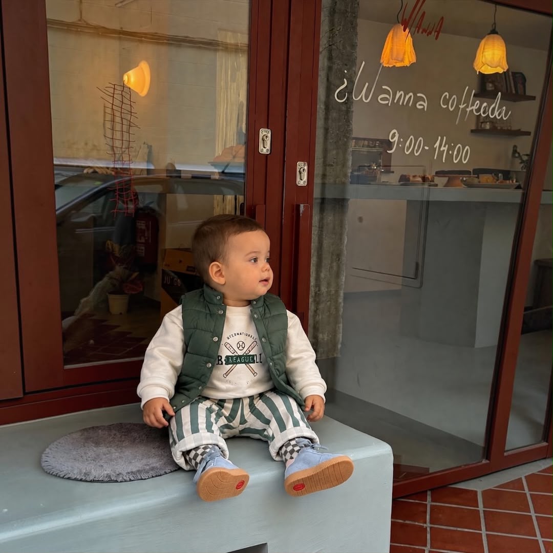 Baby boy wearing Quilted Vest Baseball Sweatshirt & Striped Pants Set sitting outside cafe