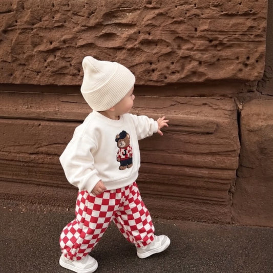 Toddler wearing teddy bear sweatshirt and red checkered joggers outdoors