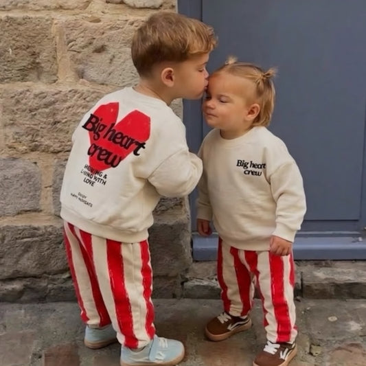 Children wearing cream Big Heart Crew sweatshirts and red striped joggers