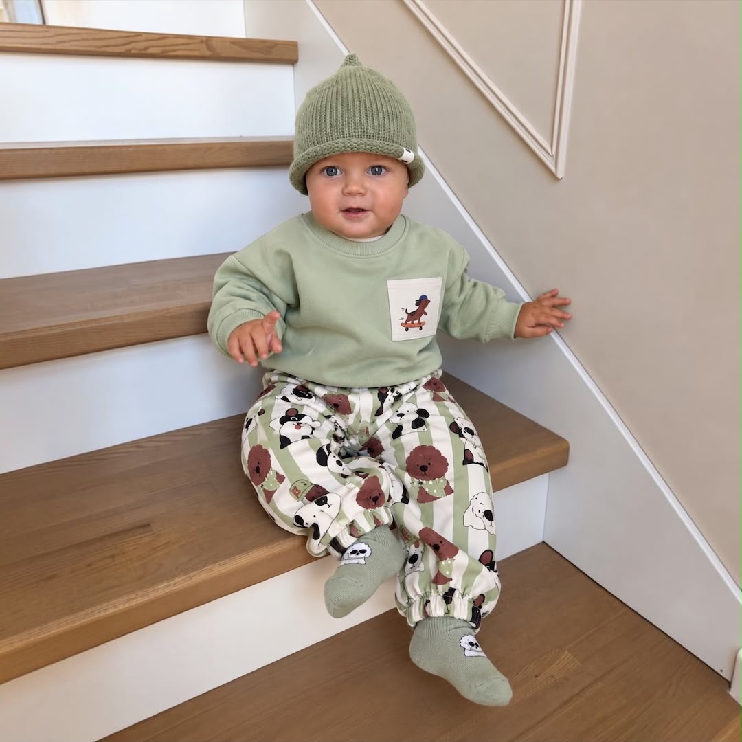 Baby wearing green dog print sweatshirt and jogger set on stairs