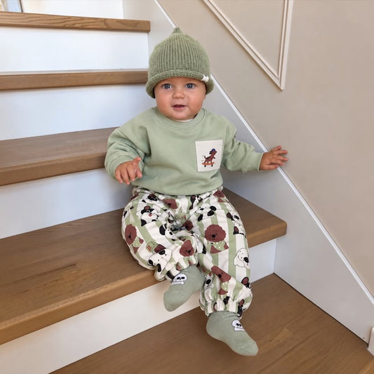Baby wearing green dog print sweatshirt and jogger set on stairs