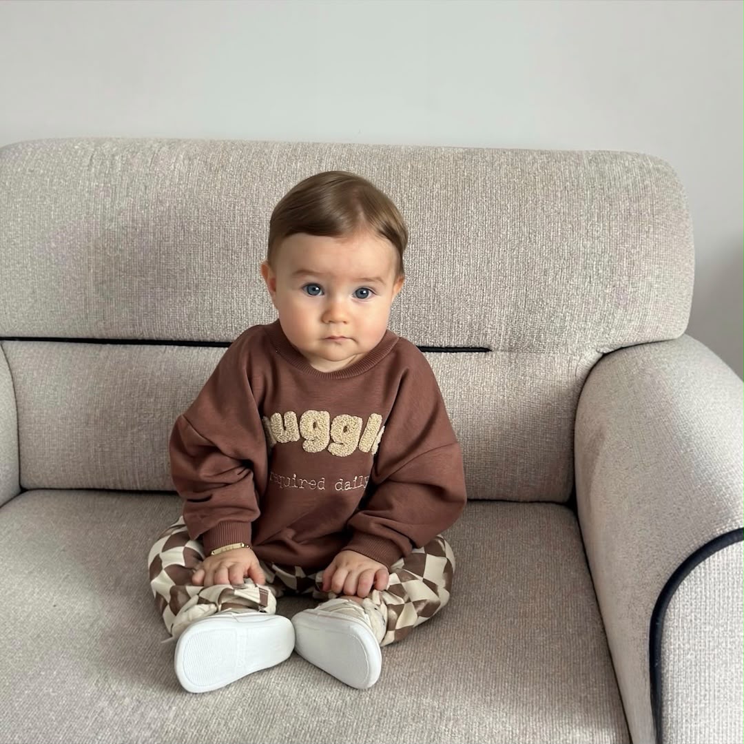Baby wearing a brown sweatshirt and checkered pants from the front