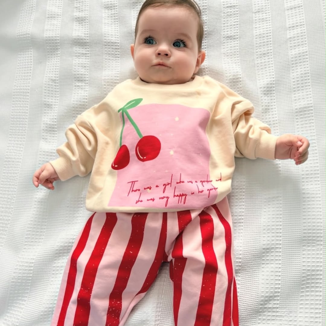 Baby lying down wearing cherry-print sweatshirt and matching striped trousers