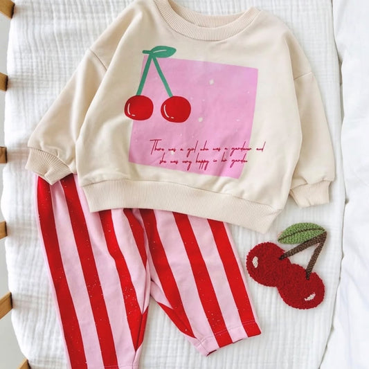 Cream cherry-print baby sweatshirt with red and pink striped trousers laid flat