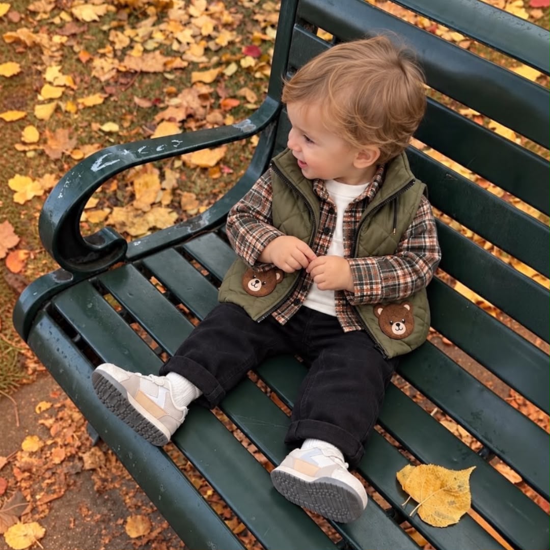 Toddler wearing olive teddy bear quilted vest plaid shirt and dark trousers outdoors