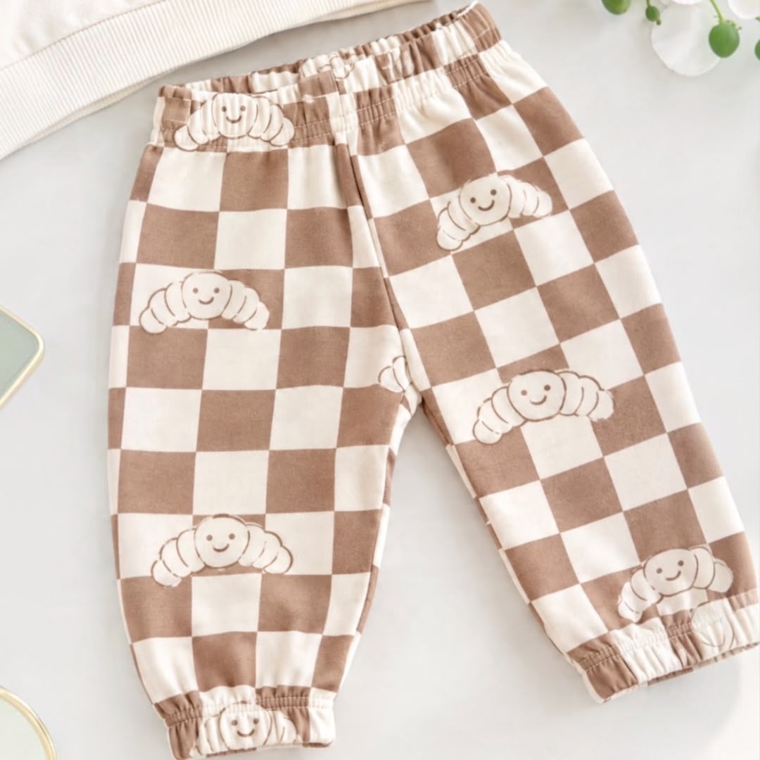 Close-up of brown and cream checkered baby joggers with smiling croissant prints