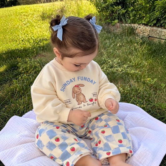 Baby wearing Sunday Funday bunny sweatshirt and strawberry checkered trousers outdoors