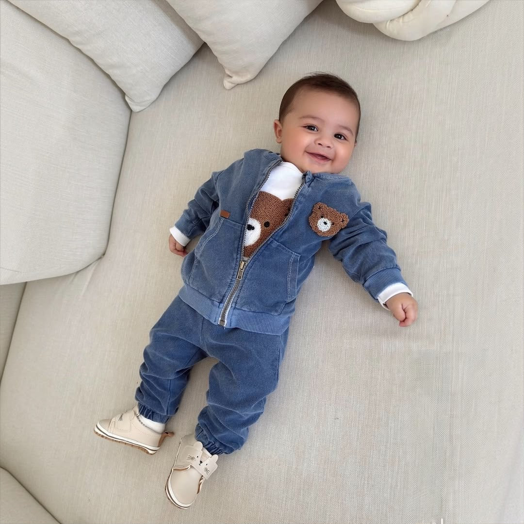 Baby boy wearing Teddy Bear Denim Zip Jacket & Jogger Set lying on cream sofa smiling