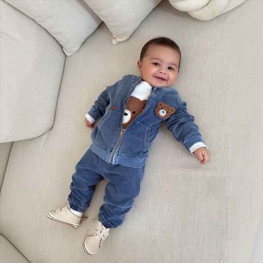 Baby boy wearing Teddy Bear Denim Zip Jacket & Jogger Set lying on cream sofa smiling