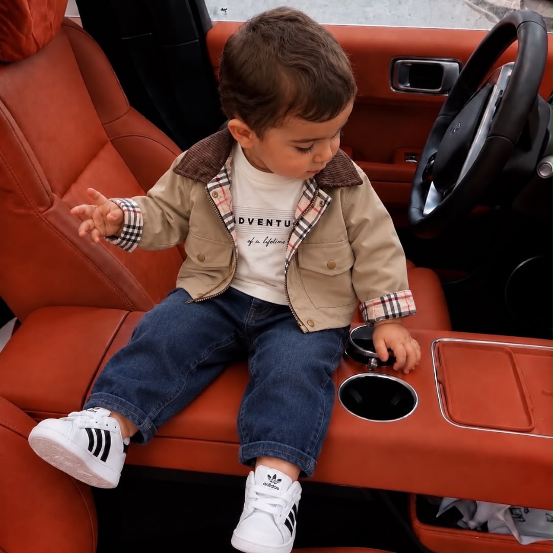 Baby boy wearing a beige jacket, printed top and blue jeans
