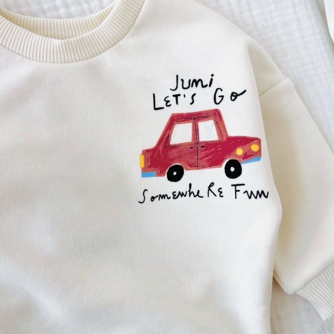 Close-up of red car graphic and lettering on cream baby sweatshirt